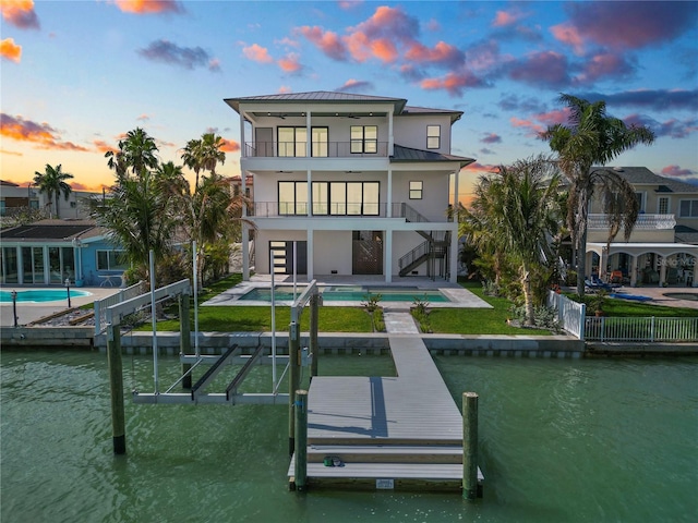 back of property with a patio, a balcony, a water view, a standing seam roof, and stairs