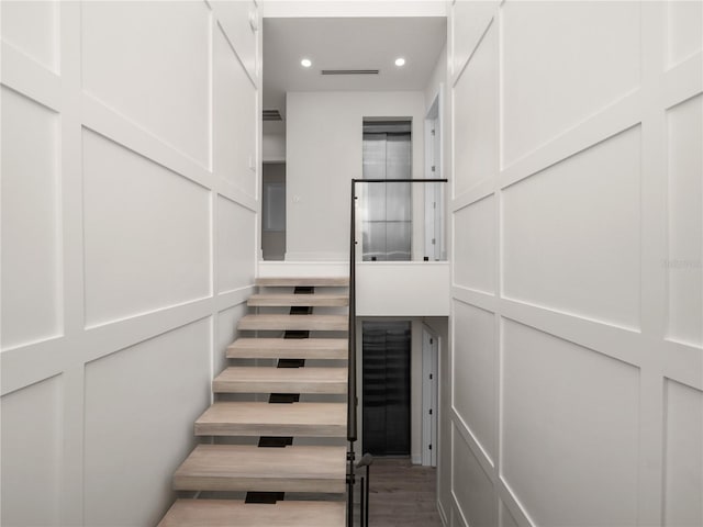stairs with recessed lighting, a decorative wall, and wood finished floors