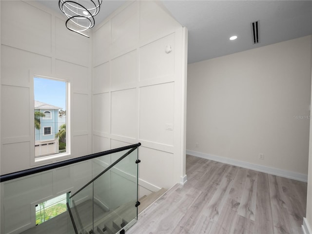 corridor featuring visible vents, a decorative wall, light wood-style floors, an upstairs landing, and baseboards