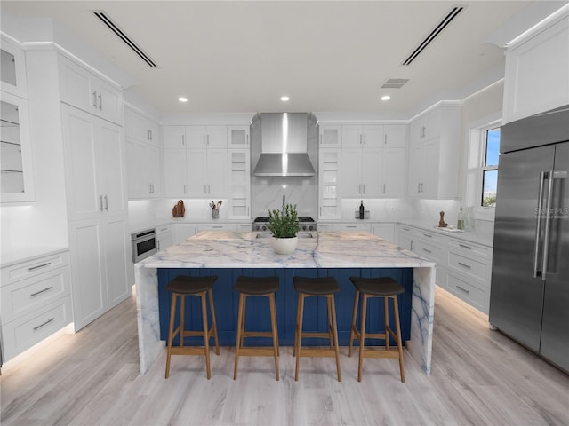 kitchen featuring high end fridge, wall chimney range hood, and visible vents