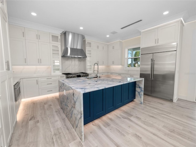 kitchen featuring built in fridge, a sink, visible vents, wall chimney range hood, and range