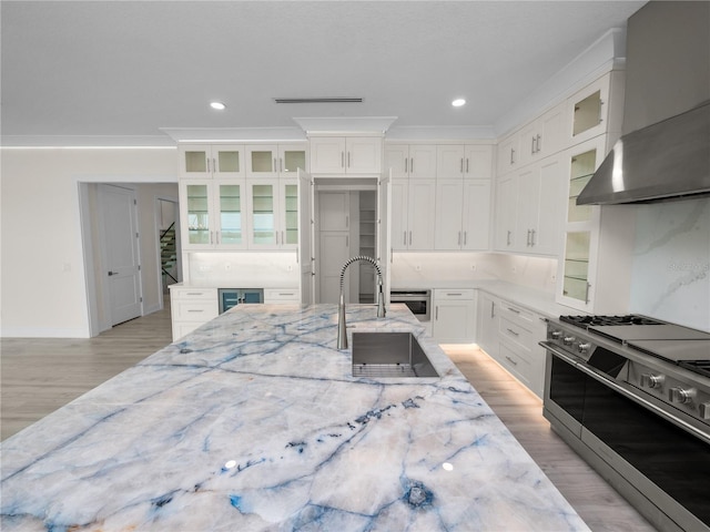 kitchen featuring light stone counters, wine cooler, appliances with stainless steel finishes, a sink, and wall chimney range hood