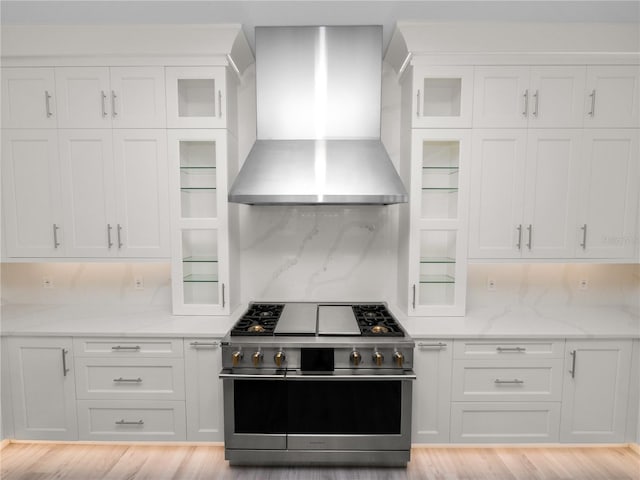 kitchen featuring high end stove, wall chimney exhaust hood, white cabinets, and backsplash