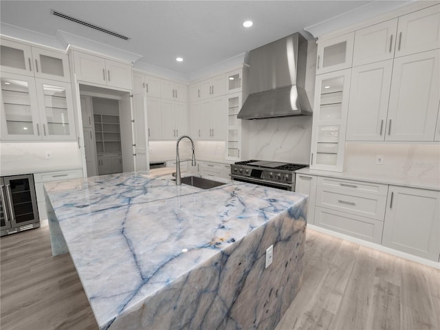 kitchen with light wood-style flooring, beverage cooler, a sink, wall chimney range hood, and double oven range