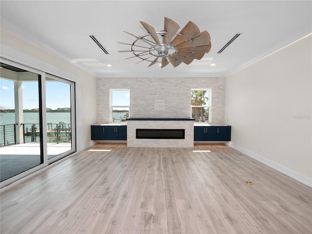unfurnished living room with light wood-style flooring, a healthy amount of sunlight, and a stone fireplace