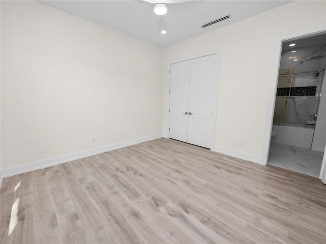 unfurnished bedroom featuring a closet, visible vents, ensuite bath, wood finished floors, and baseboards