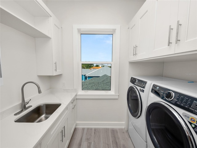 clothes washing area featuring a sink, baseboards, light wood-type flooring, independent washer and dryer, and cabinet space