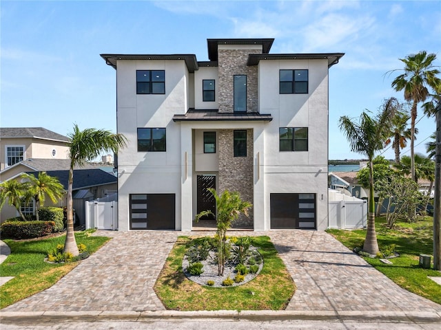 contemporary home with a garage, driveway, a standing seam roof, a gate, and stucco siding