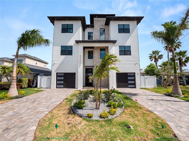 contemporary house featuring an attached garage, a gate, decorative driveway, and stucco siding