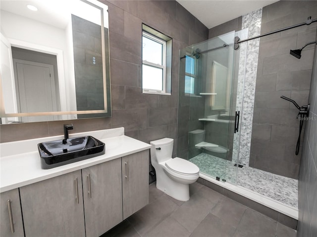 bathroom with a stall shower, toilet, tile patterned floors, vanity, and tile walls