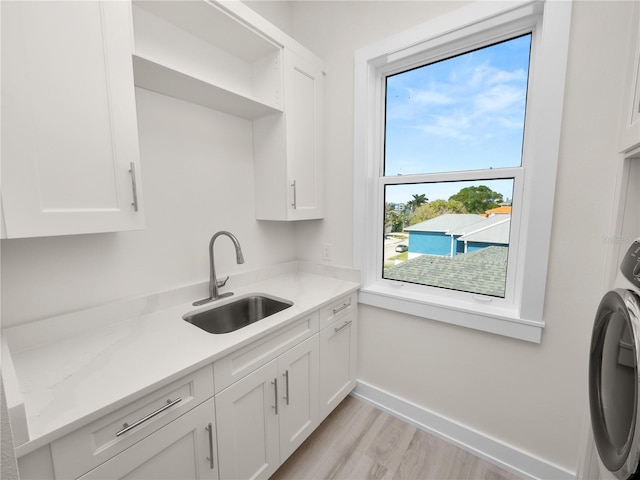 kitchen featuring a sink, baseboards, white cabinets, light countertops, and washer / clothes dryer