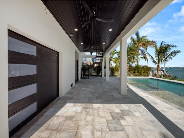 view of patio / terrace featuring stairs, ceiling fan, a water view, and an outdoor pool