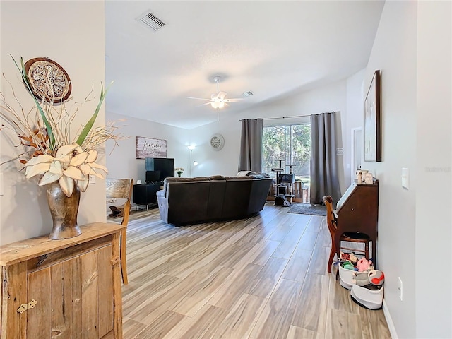 living room featuring visible vents, light wood-style floors, vaulted ceiling, ceiling fan, and baseboards