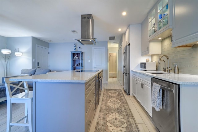 kitchen with island exhaust hood, a sink, a kitchen island, stainless steel appliances, and decorative backsplash