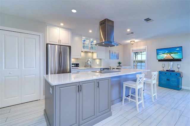 kitchen with island exhaust hood, a sink, white cabinetry, freestanding refrigerator, and decorative backsplash