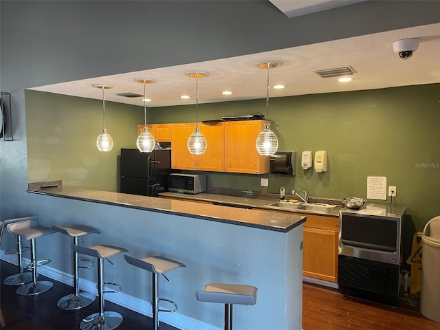 kitchen with a sink, a breakfast bar, dark wood-style flooring, and freestanding refrigerator