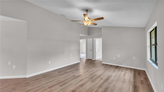 spare room featuring light wood-style floors, lofted ceiling, visible vents, and a textured ceiling