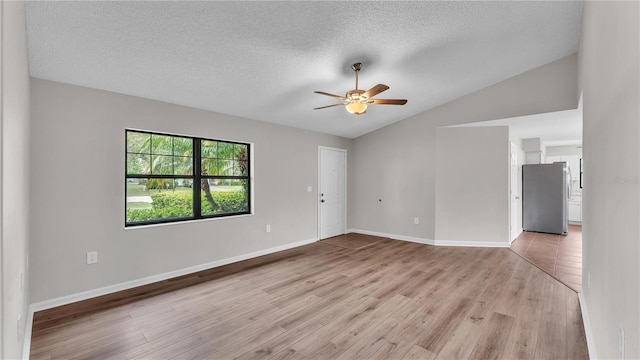 empty room with baseboards, a ceiling fan, lofted ceiling, light wood-style flooring, and a textured ceiling