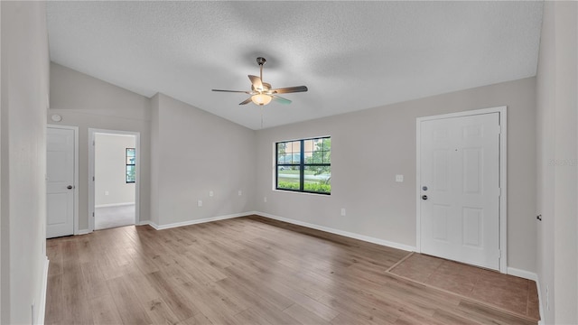 interior space featuring baseboards, lofted ceiling, ceiling fan, a textured ceiling, and light wood-style floors