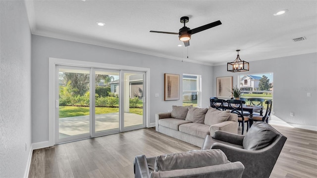 living room with visible vents, ornamental molding, wood finished floors, baseboards, and ceiling fan with notable chandelier