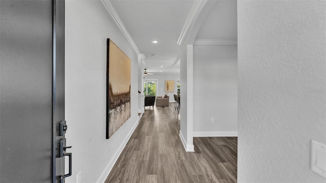 corridor featuring a textured wall, recessed lighting, wood finished floors, baseboards, and crown molding