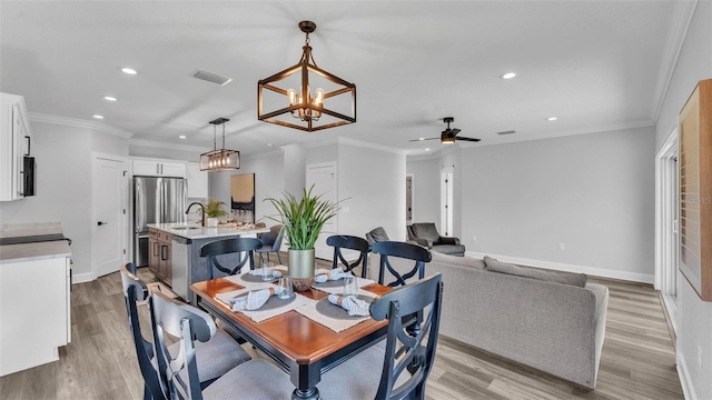 dining room with light wood finished floors, baseboards, visible vents, and crown molding