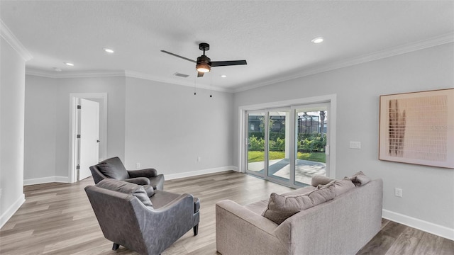 living room with a textured ceiling, ornamental molding, light wood-type flooring, and baseboards