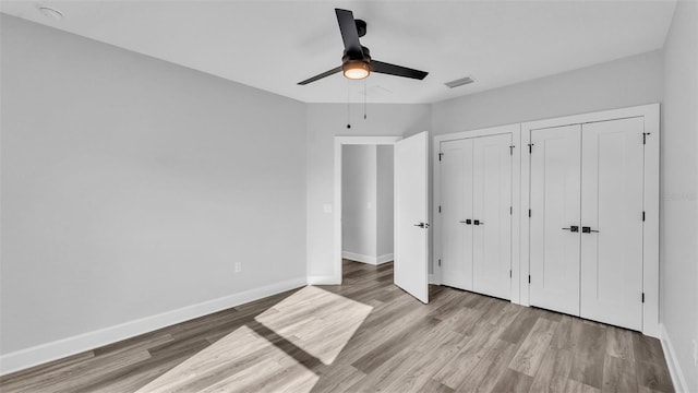 unfurnished bedroom featuring ceiling fan, baseboards, multiple closets, and wood finished floors