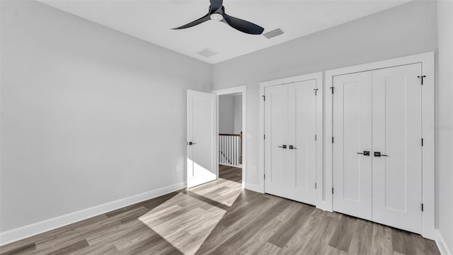 unfurnished bedroom with multiple closets, visible vents, ceiling fan, wood finished floors, and baseboards