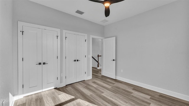 unfurnished bedroom with baseboards, visible vents, a ceiling fan, wood finished floors, and two closets