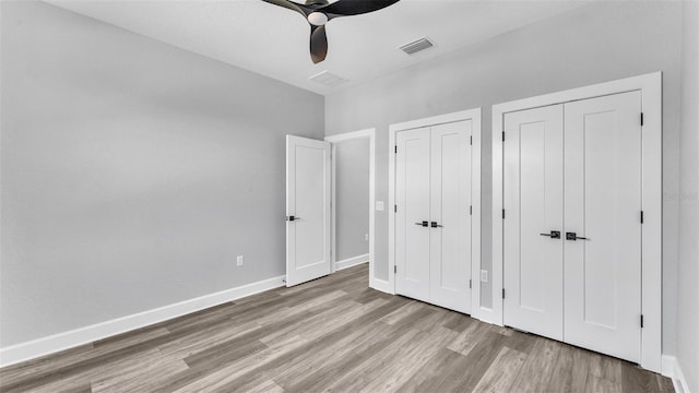 unfurnished bedroom featuring two closets, visible vents, ceiling fan, wood finished floors, and baseboards