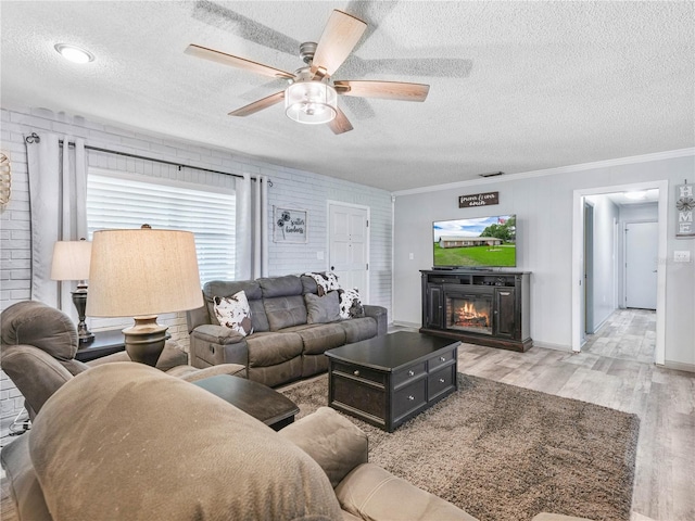 living area with visible vents, light wood-style flooring, ornamental molding, a glass covered fireplace, and a textured ceiling