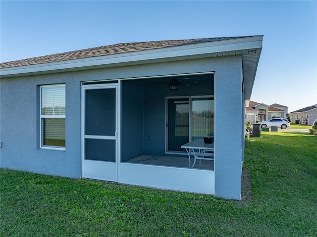 rear view of house featuring cooling unit, a sunroom, stucco siding, a shingled roof, and a lawn