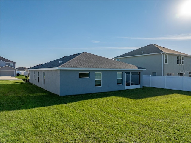 back of house with stucco siding, a lawn, a shingled roof, and fence