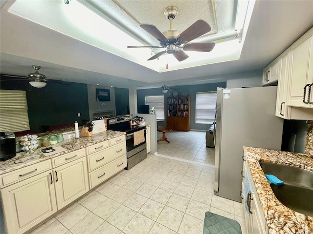 kitchen featuring a tray ceiling, appliances with stainless steel finishes, a ceiling fan, light tile patterned flooring, and a sink