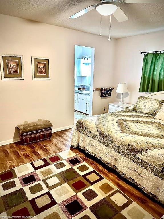 bedroom featuring a ceiling fan, ensuite bathroom, a textured ceiling, and wood finished floors