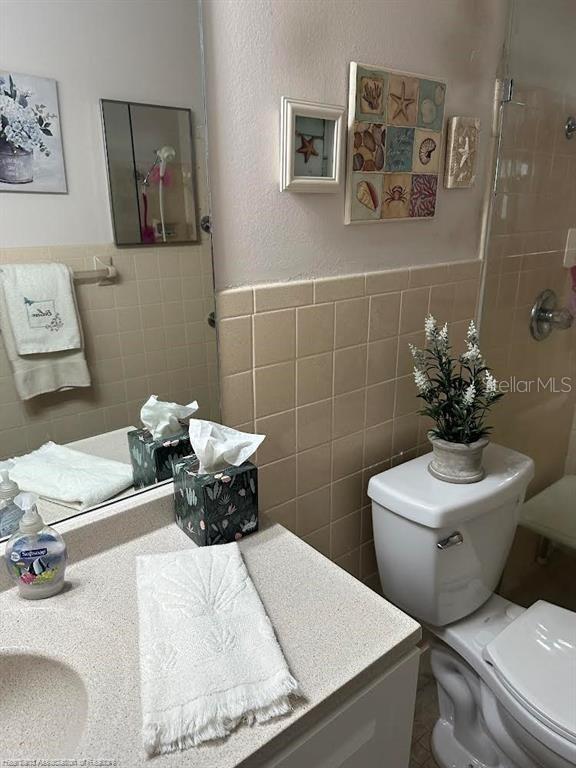 bathroom with tiled shower, tile walls, toilet, and vanity