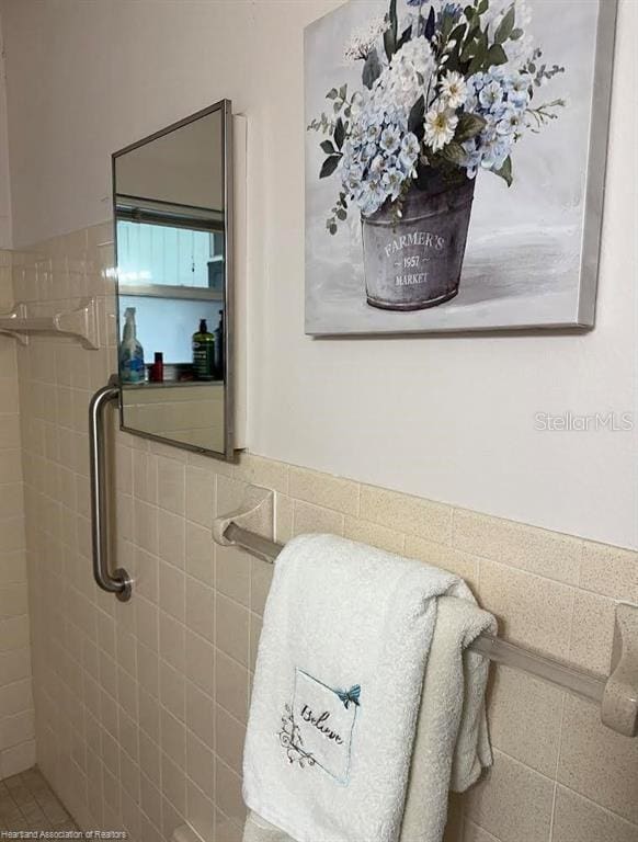 full bath featuring a wainscoted wall, tiled shower, and tile walls