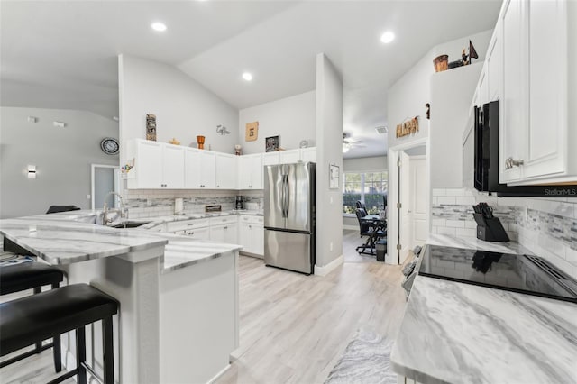 kitchen with white cabinets, freestanding refrigerator, a peninsula, light stone countertops, and a sink