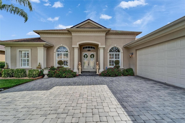 view of front of property featuring an attached garage, stucco siding, decorative driveway, and french doors