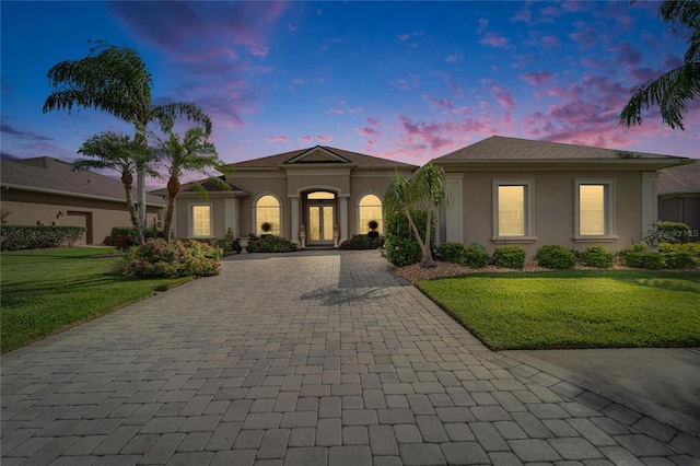 view of front of property with stucco siding, decorative driveway, and a yard