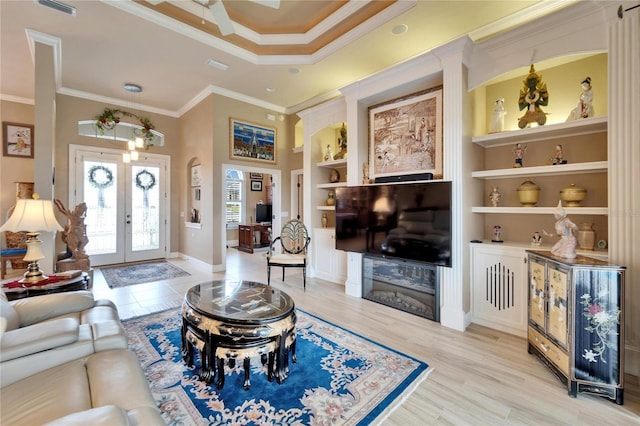 living area with a raised ceiling, ornamental molding, french doors, light wood-style floors, and built in shelves