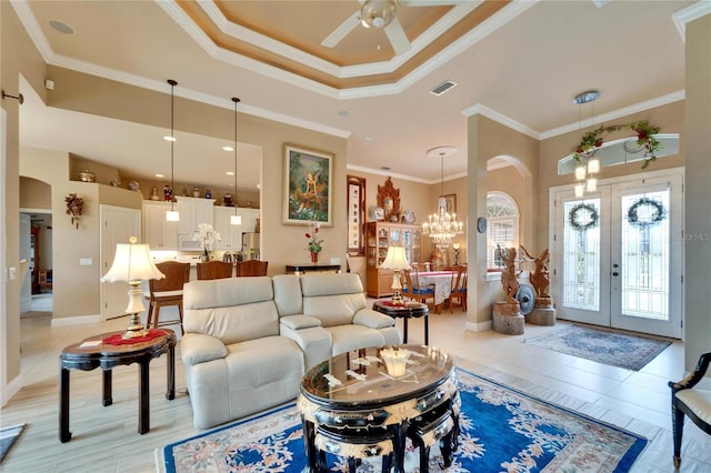 living area featuring light tile patterned floors, arched walkways, a raised ceiling, ornamental molding, and french doors