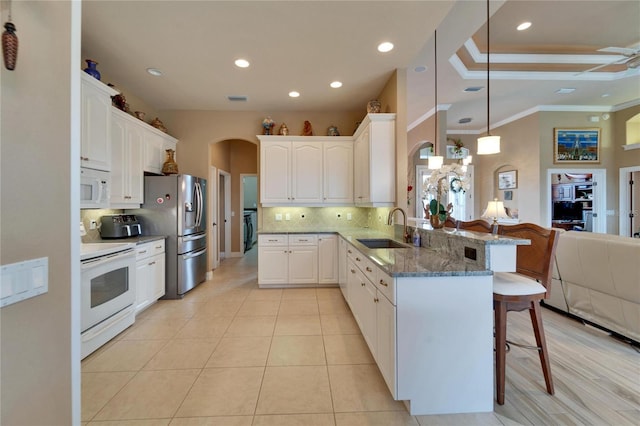 kitchen with white appliances, arched walkways, a breakfast bar area, a peninsula, and a sink