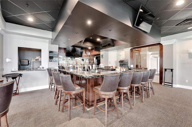 kitchen with a breakfast bar area, stone countertops, light colored carpet, a peninsula, and baseboards