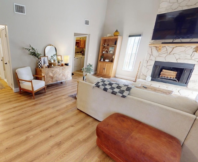 living area with a high ceiling, visible vents, wood finished floors, and a stone fireplace