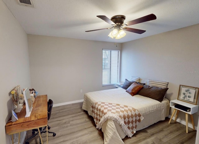 bedroom featuring visible vents, baseboards, a ceiling fan, light wood-style flooring, and a textured ceiling