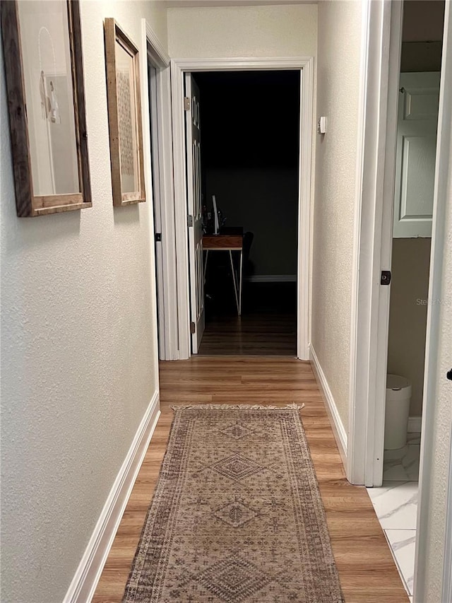 corridor with baseboards, wood finished floors, and a textured wall