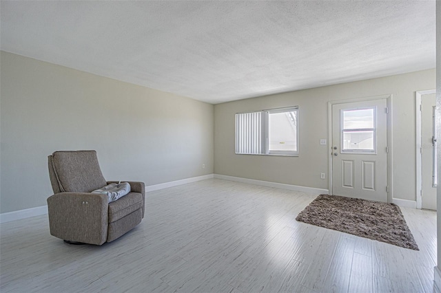 living area with light wood finished floors, baseboards, and a textured ceiling