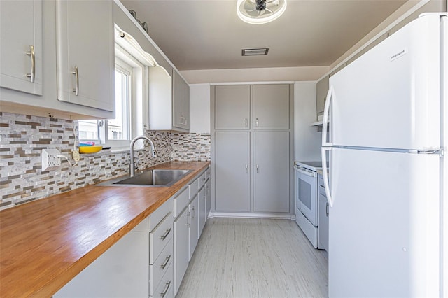 kitchen with white appliances, tasteful backsplash, visible vents, light wood-style flooring, and a sink